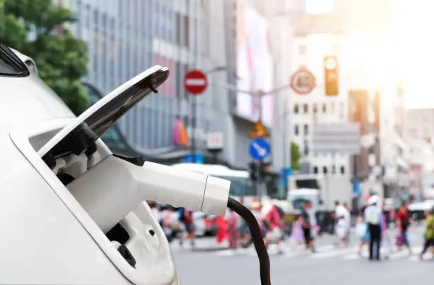 Photo of EV automotive , Air pollution and reduce greenhouse gas emissions concept.  Charging Electric car with blur city view background.