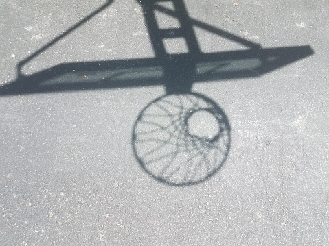 shadow of a basketball hoop with net on asphalt