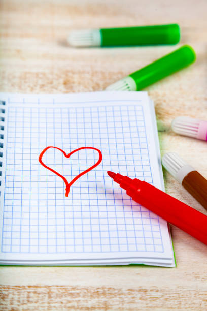 Felt pens and notebook. Red heart is drawn on a checkered sheet.