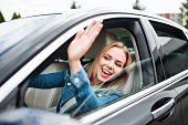 Young woman driver sitting in car, greeting somebody.