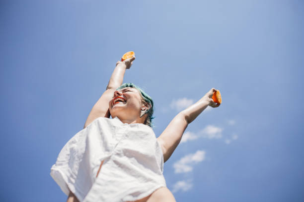 mulher nova feliz com laranjas - arms raised people orange blue - fotografias e filmes do acervo