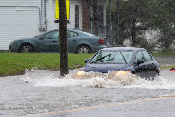 Saint John, NB, Canada - September 7, 2019: A car drives through water on a flooded road. The flood was caused by wind and rain from Hurricane Dorian. Rain visible in the air (it is not noise).