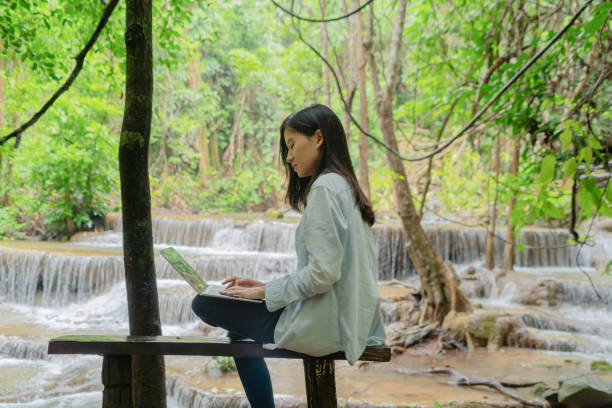 istock Happy Asian woman, a freelance, working and using a computer laptop notebook at waterfall in the tropical forest during travel trip and holidays vacation outdoors at national park, Thailand. 1173178616