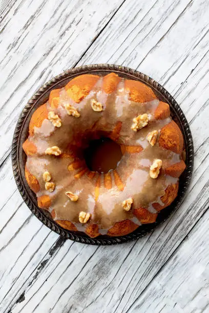 Delicious, Pumpkin Spice Bundt Cake frosted with brown sugar frosting and walnuts oven a rustic wood table background.  Top down view.