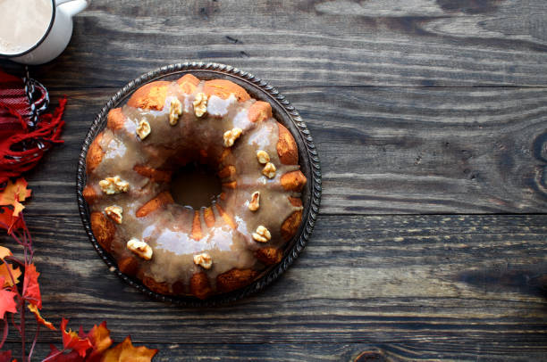 Delicious, Pumpkin Spice Bundt Cake frosted with brown sugar frosting and walnuts with Autumn leaves and coffee over a rustic woode table background. Image shot from top view..