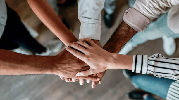 Cooperation. Top view of people holding hands together while standing in the office stock photo