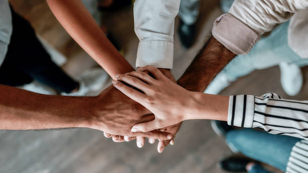 cooperation. top view of people holding hands together while standing in the office - holding hands imagens e fotografias de stock