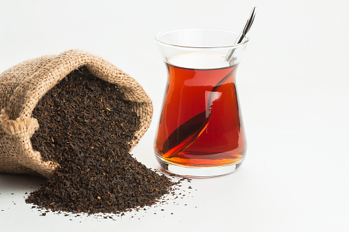 Glass Turkish brewed black tea and dry black tea in burlap sack isolated on white background. Turkish traditional hot drink