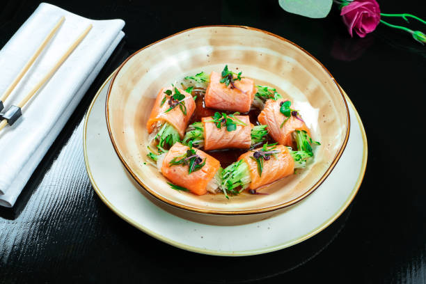 istock Close up on creative made sushi roll with salmon, microgreen, cucumber. Delicious salmon sashimi in yellow bowl with soy sauce on dark background. Japanese cuisine. Seafood, raw fish. 1173187408