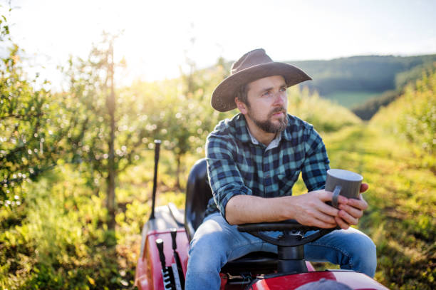 Confident young man driving a tractor across farmland, engaged in agricultural work. Rural lifestyle and hands-on farming in a natural outdoor setting.