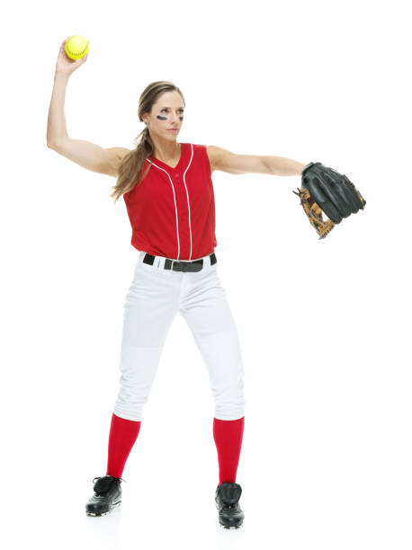 lunghezza intera / vista laterale / vista del profilo di 20-29 anni adulto bellissimi capelli castani / capelli lunghi caucasici femmina / giovane donna softball giocatore / atleta / lanciatore softball / lanciatore in piedi di fronte allo sfondo bianco e  - softball adult catching beautiful foto e immagini stock