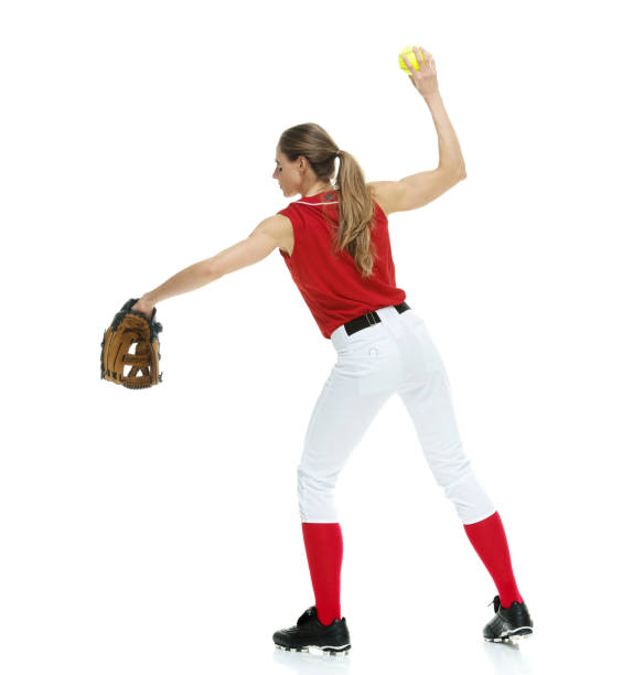 lunghezza intera / vista laterale / vista del profilo di 20-29 anni adulto bellissimi capelli castani / capelli lunghi caucasici femmina / giovane donna softball giocatore / atleta / lanciatore softball / lanciatore in piedi di fronte allo sfondo bianco e  - softball adult catching beautiful foto e immagini stock