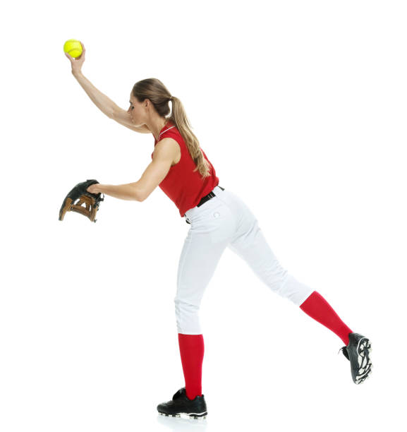 lunghezza intera / vista laterale / vista del profilo di 20-29 anni adulto bellissimi capelli castani / capelli lunghi caucasici femmina / giovane donna softball giocatore / atleta / lanciatore softball / lanciatore in piedi di fronte allo sfondo bianco e  - softball adult catching beautiful foto e immagini stock