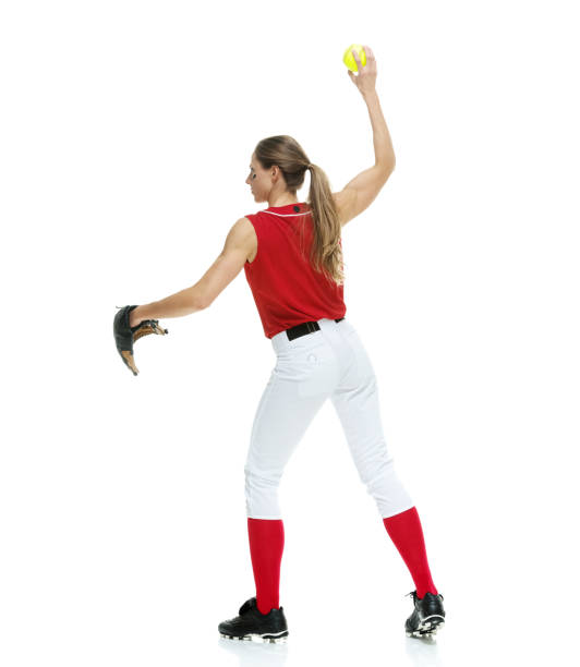 lunghezza intera / vista laterale / vista del profilo di 20-29 anni adulto bellissimi capelli castani / capelli lunghi caucasici femmina / giovane donna softball giocatore / atleta / lanciatore softball / lanciatore in piedi di fronte allo sfondo bianco e  - softball adult catching beautiful foto e immagini stock