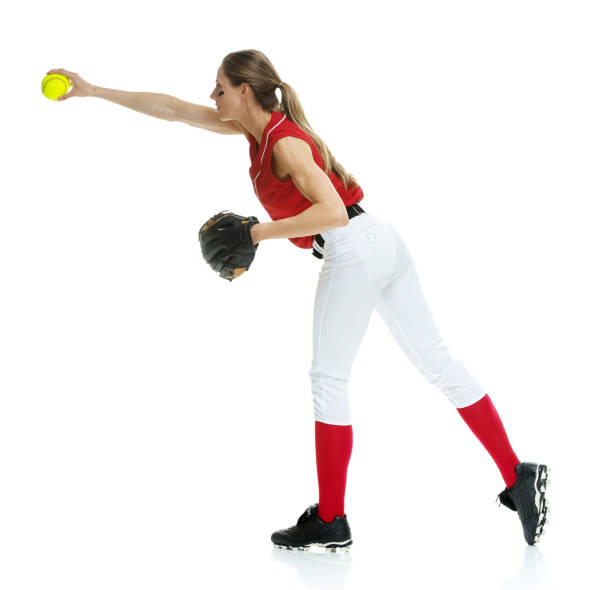 lunghezza intera / vista laterale / vista del profilo di 20-29 anni adulto bellissimi capelli castani / capelli lunghi caucasici femmina / giovane donna softball giocatore / atleta / lanciatore softball / lanciatore in piedi di fronte allo sfondo bianco e  - softball adult catching beautiful foto e immagini stock