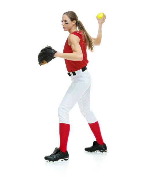 lunghezza intera / vista laterale / vista del profilo di 20-29 anni adulto bellissimi capelli castani / capelli lunghi caucasici femmina / giovane donna softball giocatore / atleta / lanciatore softball / lanciatore in piedi di fronte allo sfondo bianco e  - softball adult catching beautiful foto e immagini stock