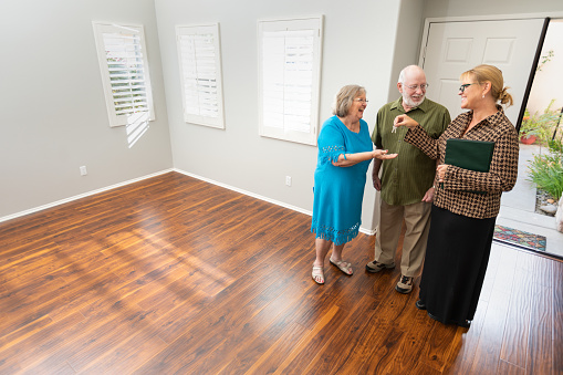 Female Real Estate Agent Handing New House Keys to Senior Adult Couple In New Home.