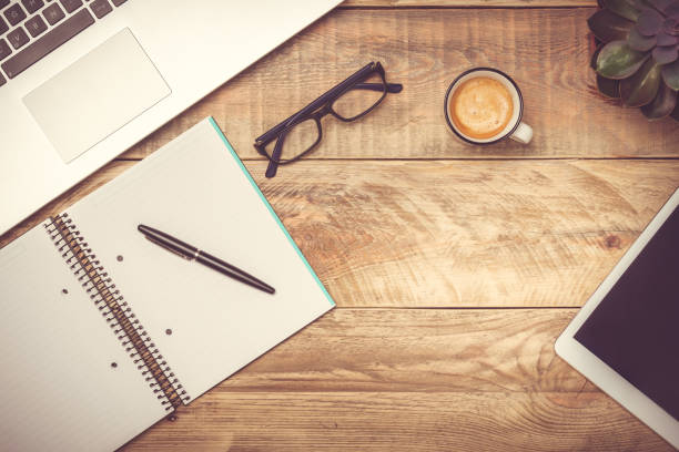 istock Rustic wooden desk with laptop, notebook, pen, glasses, coffee cup and tablet computer. Modern workspace with copy space. Filter toning effect. 1173194372