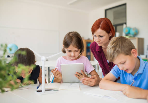 istock Group of small school kids with teacher sitting in circle in class, using tablet. 1173196948