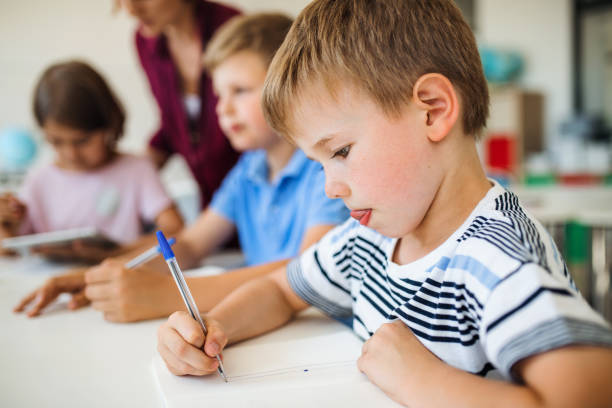 группа маленьких школьников с учителем в классе письменной форме. - school child education furniture стоковые фото и изображения