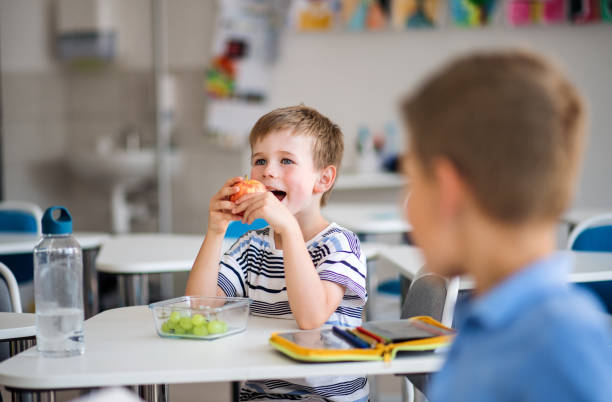 Small school children sitting at the desk in classroom, eating fruit. Small school children sitting at the desk in classroom, eating fruit for snack. food elementary student healthy eating schoolboy stock pictures, royalty-free photos & images