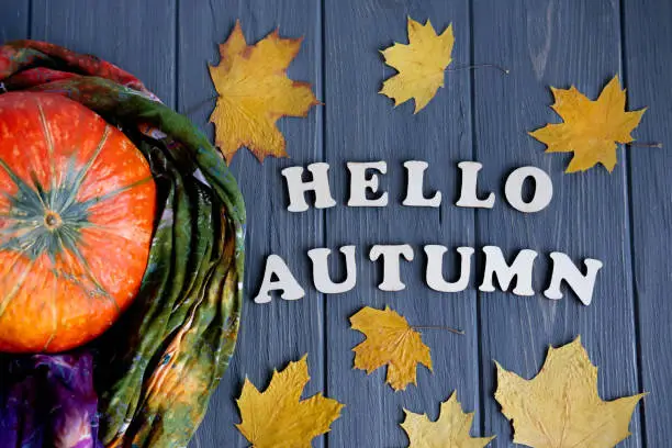 Photo of Lettering Hello Autumn from wooden letters. Autumn banner with pumpkin and autumn yellow leaves on a gray wooden background