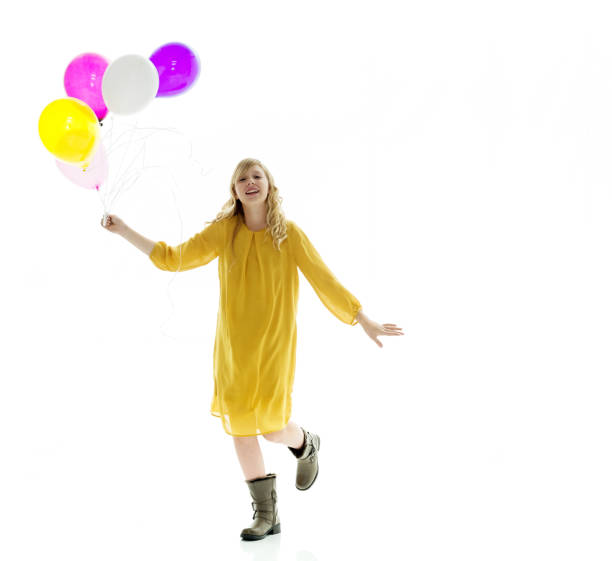 full length / front view / looking at camera of 10-11 years old beautiful blond hair / long hair caucasian / generation z young women / female teenage girls standing in front of white background wearing dress / boot who is smiling / happy / cheerful - 10 11 years cheerful happiness fun imagens e fotografias de stock