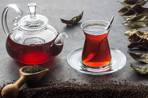 Glass Turkish brewed black tea and glass teapot with dry black tea and dried tea leaves on black rustic table. Turkish traditional hot drink