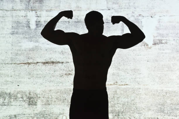 One man only / waist up / front view of 30-39 years old adult handsome people / short hair latin american and hispanic ethnicity male / young men athlete / sportsperson standing in front of gray background / black background who is outdoors wearing sports clothing who is serious / confidence / concentration and showing flexing muscles with shadow / back lit / silhouette / concrete / wall - building feature / black color un hombre sólo / cintura para arriba / vista frontal de 30-39 años de edad adulto guapo personas / pelo corto latino y etnia hispana hombre / hombres jóvenes atleta / deportista de pie frente a fondo gris / fondo negro que está al aire libre