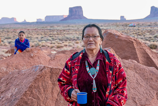 Navajo Grandmother and Granddaughter posing together in front of The Mittens Rock Formations in the Monument Valley Tribal Park in Arizona