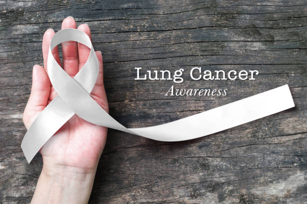 Lung cancer awareness month with white/ light pearl color ribbon on woman's hand support on aged wood Lung cancer awareness month with white/ light pearl color ribbon on woman's hand support on aged wood osteoporosis awareness stock pictures, royalty-free photos & images