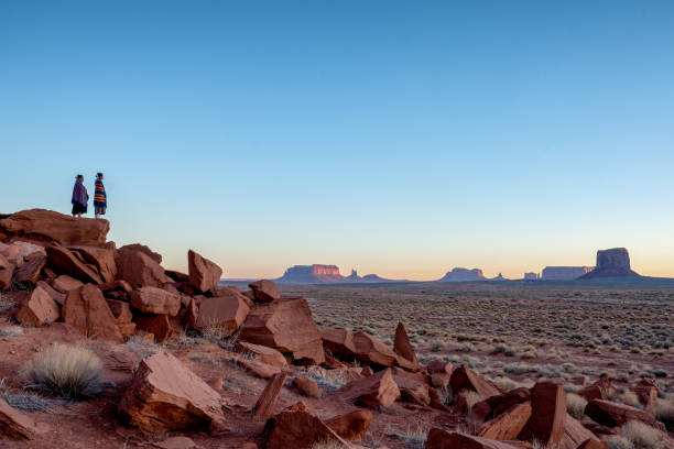 Two Teenage Native American Indian Navajo Sister in Traditional Clothing Enjoying the Vast Desert and Red Rock Landscape in the Famous Navajo Tribal Park in Monument Valley Arizona at Dawn Two Teenage Native American Indian Navajo Sister in Traditional Clothing Enjoying the Vast Desert and Red Rock Landscape in the Famous Navajo Tribal Park in Monument Valley Arizona at Dawn navajo stock pictures, royalty-free photos & images