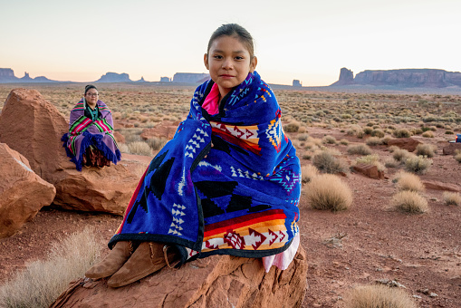 Two Teenage Native American Indian Navajo Sister in Traditional Clothing Enjoying the Vast Desert and Red Rock Landscape in the Famous Navajo Tribal Park in Monument Valley Arizona at Dawn