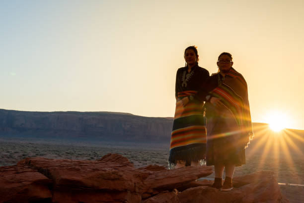 Two Teenage Native American Indian Navajo Sister in Traditional Clothing Enjoying the Vast Desert and Red Rock Landscape in the Famous Navajo Tribal Park in Monument Valley Arizona at Dawn Two Teenage Native American Indian Navajo Sister in Traditional Clothing Enjoying the Vast Desert and Red Rock Landscape in the Famous Navajo Tribal Park in Monument Valley Arizona at Dawn hopi culture photos stock pictures, royalty-free photos & images
