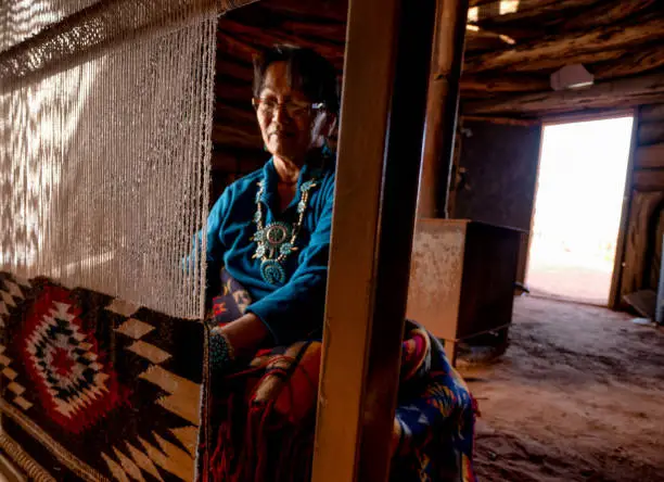 Native american navajo woman in an authentic hogan weaving a traditional blanket on a loom