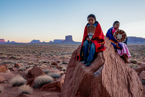 Joven navajo hermano y hermana en Monument Valley posando en rocas rojas frente a las increíbles formaciones de Mittens Rock en el desierto al amanecer photo