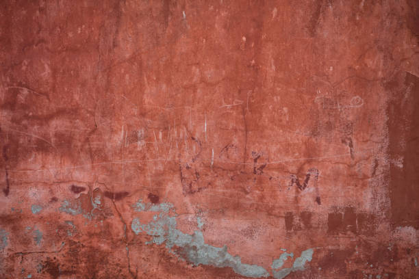 Red plaster wall with pealing paint and exposed concrete. scratches stock photo