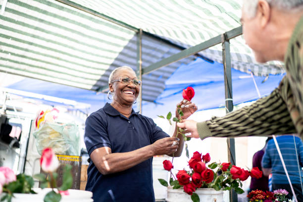 florista sênior que vende uma rosa ao cliente - men african descent giving flower - fotografias e filmes do acervo