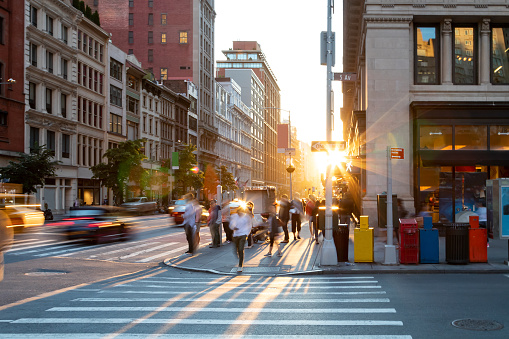 Man walking through the crosswalk at the busy intersection of 5th Avenue and 23rd Street in New York City with bright light of sunset in the background