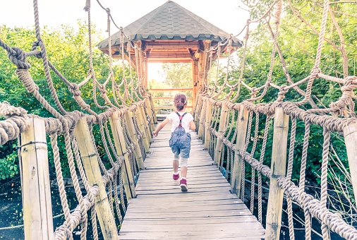 Little girl running away at suspension bridge above water