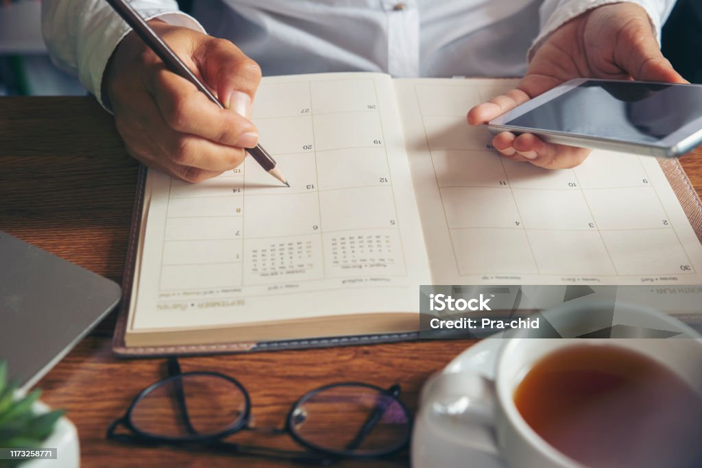 Female'hand of planner writing daily appointment. On 2020 Calendar book,Female'hand of planner writing daily appointment.Woman mark and noted schedule(holiday trip) on diary at office desk.Calendar reminder event for planner concept Personal Organizer Stock Photo