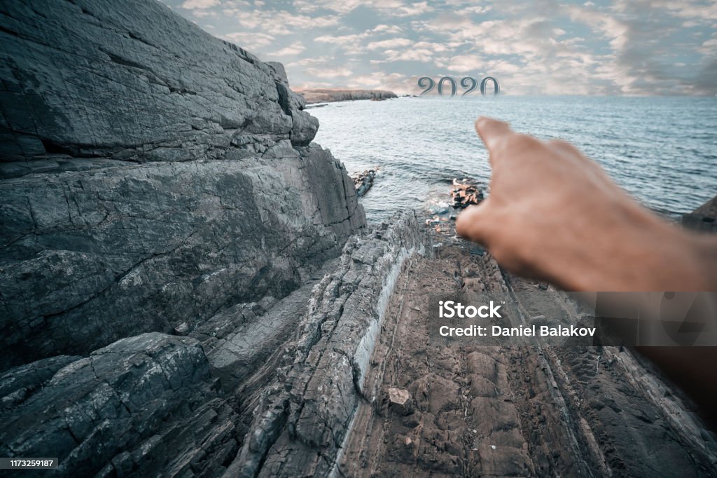 Happy New Year at the sea. 2020-New year concepts-stock photo A man's hand at a rocky coast pointing at the horizon where the new year 2020 is coming... New Year Card Stock Photo