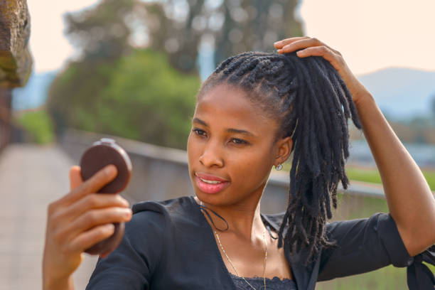 Portrait of an stylish young African woman checking her face in a small compact mirror