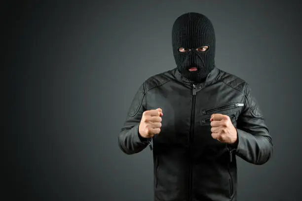 Robber, thug in a balaclava on a black background. Robbery, hacker, crime, theft. Copy space