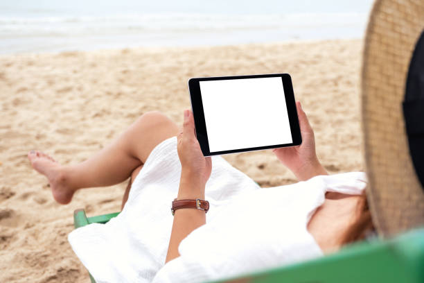 istock a woman holding a black tablet pc with blank desktop screen while lying down on a beach chair 1173268370