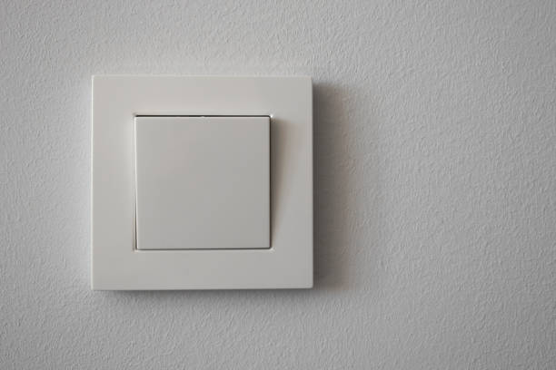 White plastic light switch on light gray wall, close-up. Copy space. stock photo