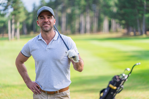 Waist up image of adult golf player standing leisurely on the golf course and looking at camera