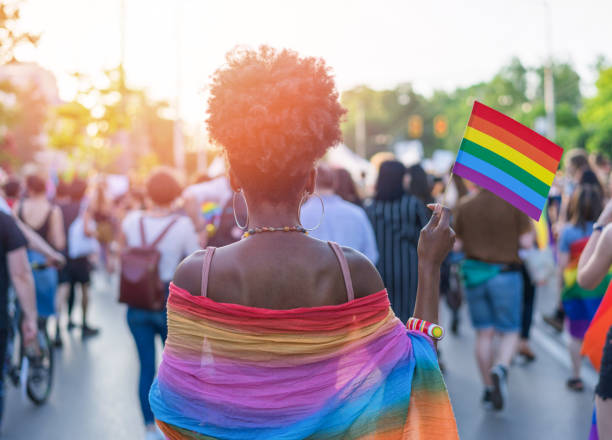 Young African ethnicity woman at the love festival Rear view image of young African-American woman walking at the LGBTQI pride event and waving rainbow flag gay pride people stock pictures, royalty-free photos & images