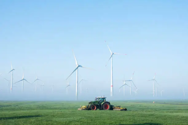 farmer mows grass near wind turbine farm in oastfriesland on misty summer morning in german ostfriesland
