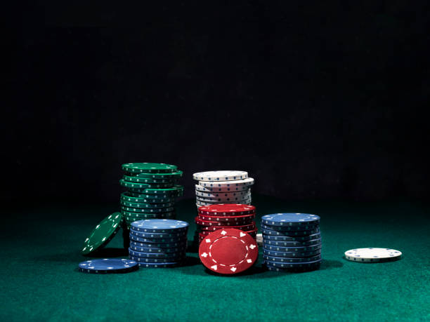 primo primo scatto di una pila di patatine colorate, alcune delle quali giacevano nelle vicinanze sulla copertina verde del tavolo da gioco. sfondo nero. primo piano - poker foto e immagini stock